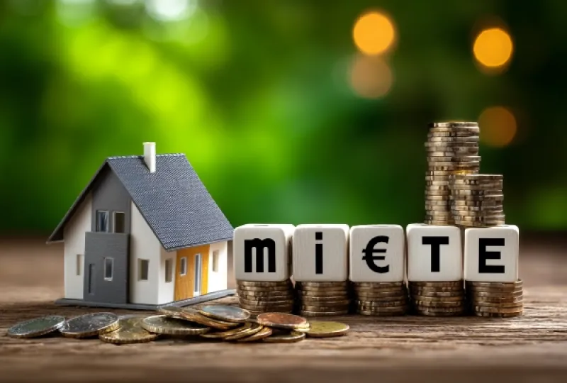 Symbolbild: Modellhaus mit Münzen auf die Würfel mit der Aufschrift "Miete"gestellt sind