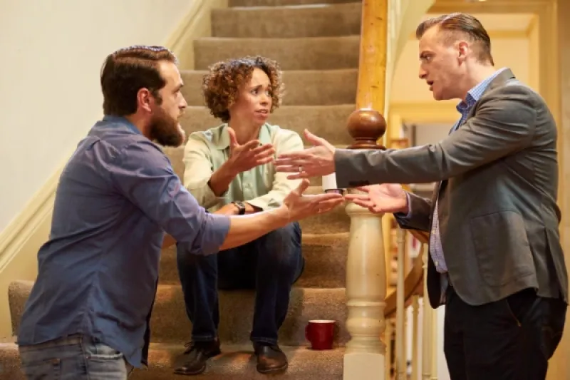 zwei Männer streiten im Treppenhaus, eine Frau sucht zu vermitteln