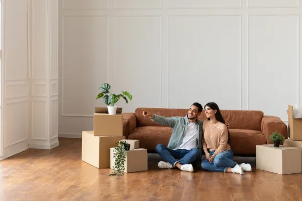 junges Paar sitzt neben Kartons vor dem Sofa und schaut zum Fenster
