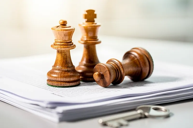 Symbolbild: Drei Schachfiguren auf einem Papierstapel, eine ist umgefallen