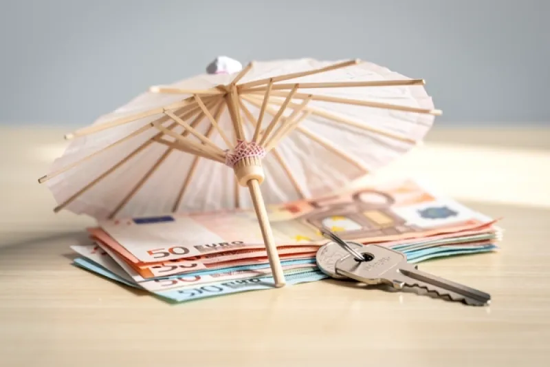 Symbolbild: Papierschirm über Eurobanknoten und einem Hausschlüssel