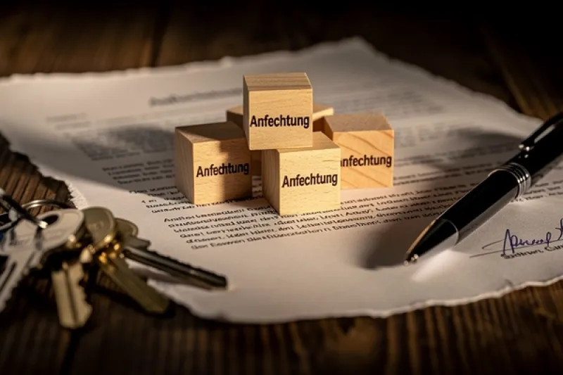 Symbolbild: Holzwürfel mit dem Wort 'Anfechtung' stehen auf einem zerrissenen Blatt Papier